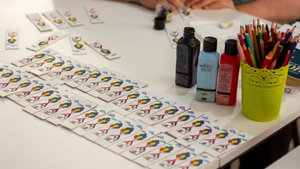 Close-up of crafting setup with playing cards, paints, and pencils on a table.