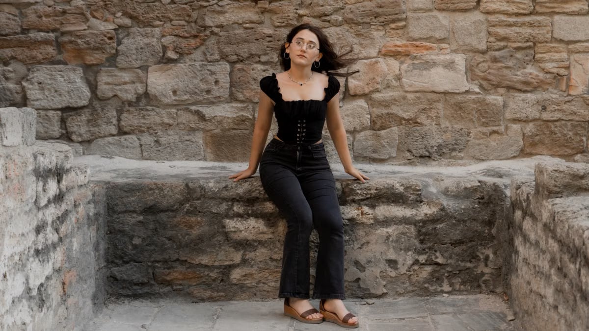 A woman in stylish attire seated on a historic stone wall in Baku, exuding elegance and confidence.